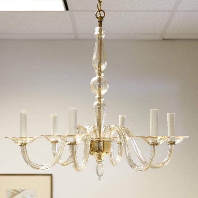 A champagne colored Murano glass chandelier featuring 6 scroll form arms, each ending in a glass bobeche and candle style...
