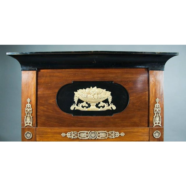 Rectangular with ebonized cornice over a panel with central cornucopia over a mirror plate with a conforming bronze...