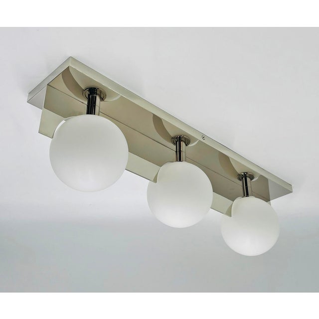 Modern three-light wall sconce or vanity fixture featuring a sleek chromed metal frame and three large frosted glass globe...