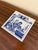 A classic Dutch Delft-style hand painted blue and white porcelain tile featuring a scene of Herbalists in rich cobalt blue...
