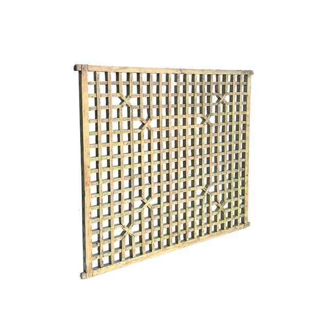 This image features a vintage wooden lattice panel, painted in a faded, mustard-yellow hue that speaks to its age and...