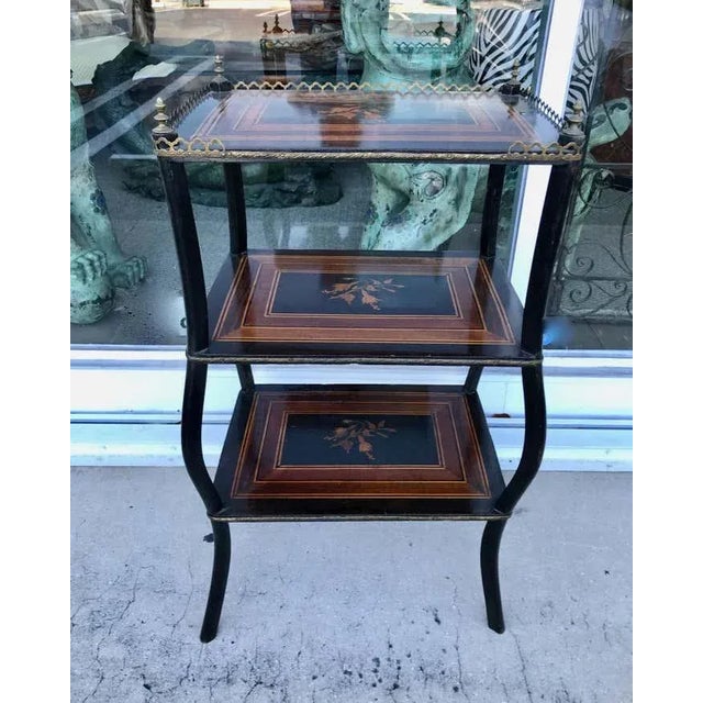 The stand is fashioned with 3 inlaid shelves, an upper brass gallery, together with brass banding and finials. [ height...