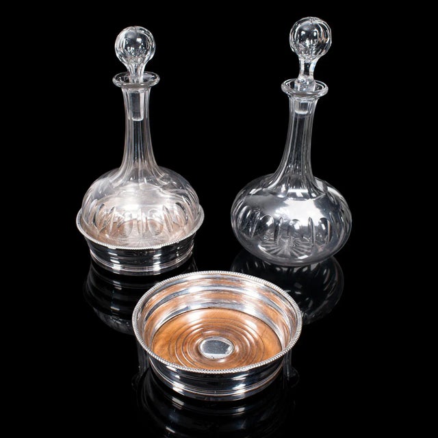 This is a pair of antique decanters with stands. An English, glass vessel and silver plate coaster, dating to the...