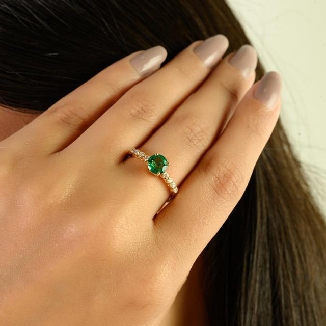 This certified 14K yellow gold ring featuring a vivid round-cut natural Zambian emerald weighing approximately 0.57...