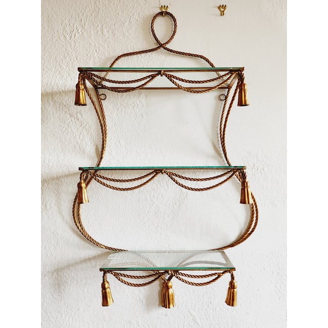 Vintage Italian Mid-Century Hollywood Regency style large gilt iron wall mounted shelf with a rope and tassel motif. Each...