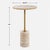 This accent table features a travertine top and base supported by a metal stem in a rich brass finish. The combination of...
