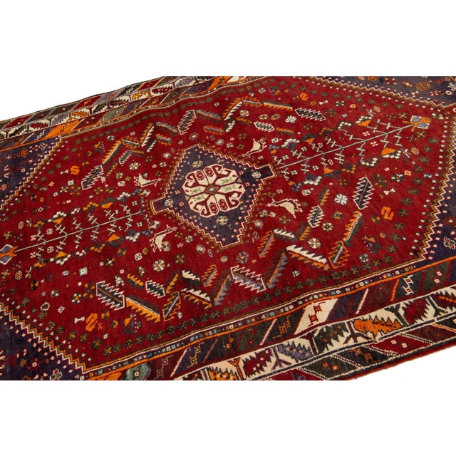 This Vintage Shiraz hand-knotted wool rug has a red field with multicolor accents all over the motif. This rug measures...