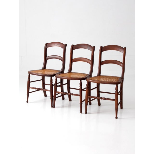 This set of three antique cane dining chairs dates to the late 19th to early 20th century. Warm wood frames pair with...