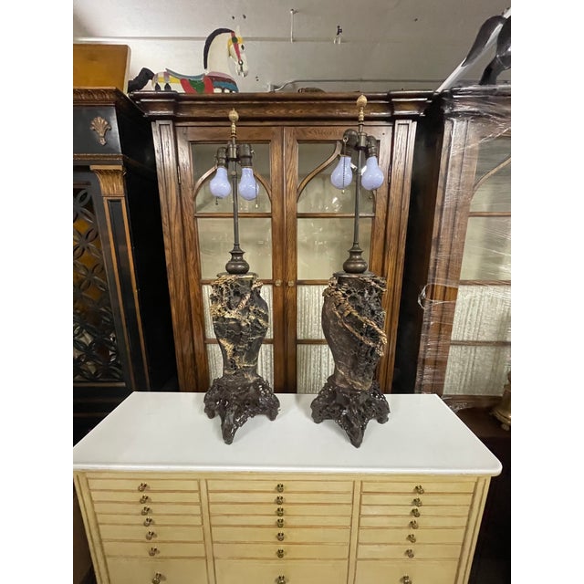 A pair of antique Chinese table lamps in a dark brown soapstone with streaks of lighter, cream-colored veins that are...