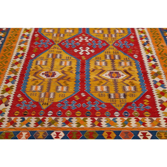 A contemporary Kilim rug showcases an exuberant and detailed geometric motif throughout the red field, employing a variety...