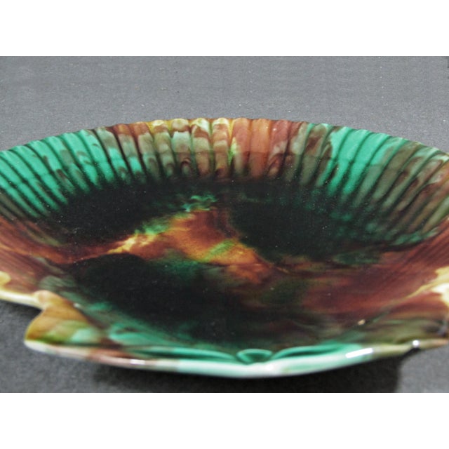 An antique 19th-century Wedgwood majolica scallop-shell shaped plate with mottled green, brown, amber, and cream glaze....