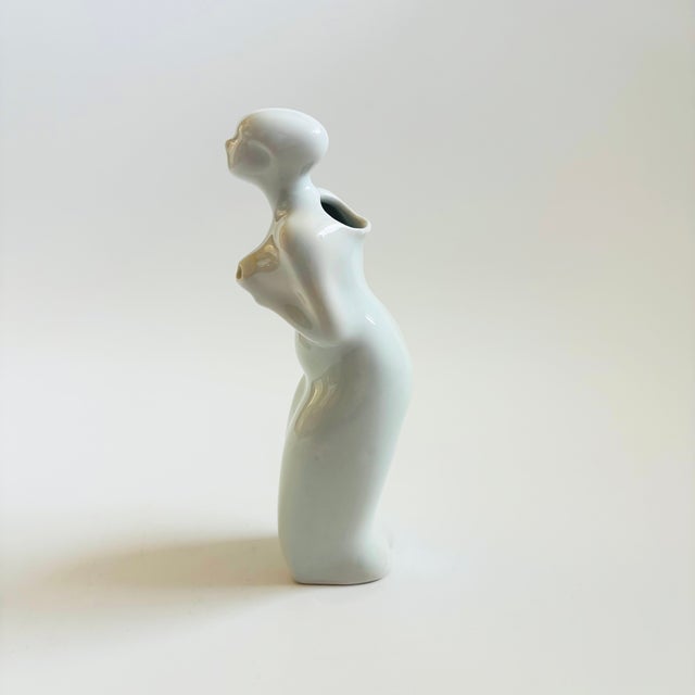 A vintage porcelain creamer or milk pitcher in the shape of a woman. There is a hole on the back for filling and a hole in...