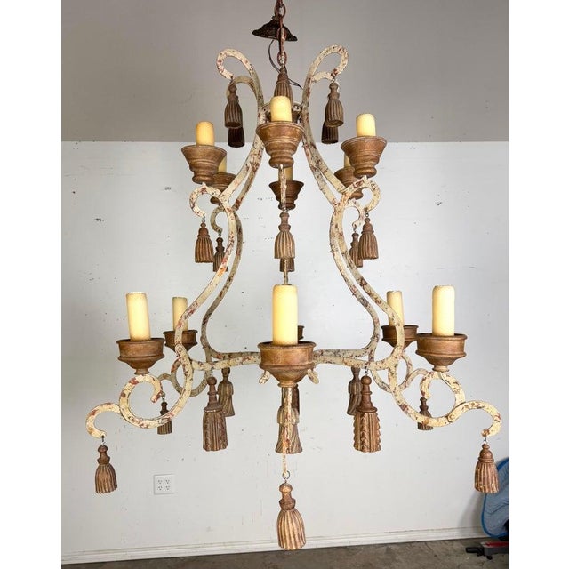 French Provincial style two-tier wrought iron chandelier adorned with gilt tassels. The hand forged frame features an...