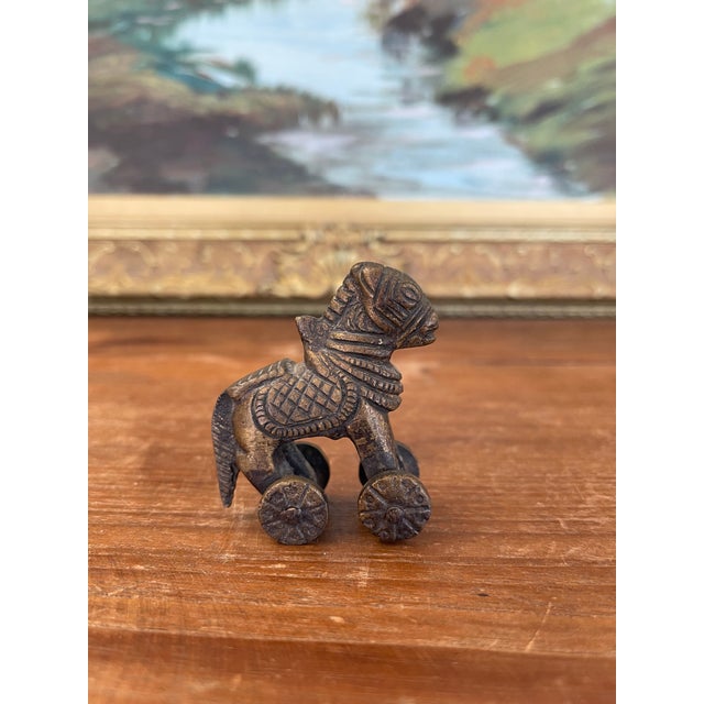 Small likely antique bronze toned figurine depicting a stylized horse mounted on four functional wheels.Likely originating...
