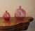 A pair of two amaranth pink blown glass vases in varying sizes. The vases are identical but different sizes. They are...