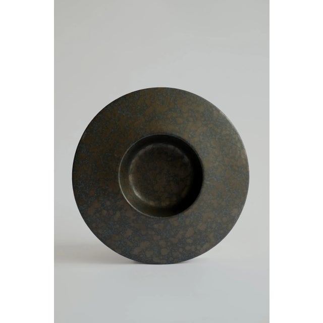 Wheel-thrown ceramic shallow vessel with a wide, sculptural rim, finished in a richly mottled, iron-toned glaze. The...