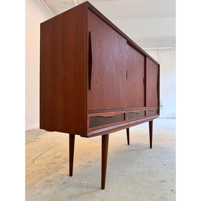 This Danish highboard from the mid-century era is a true masterpiece of Scandinavian storage solutions, captivating with...