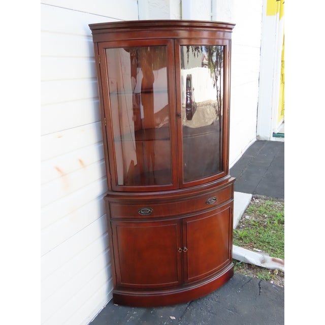 This elegant corner cabinet is crafted from wood, solid mahogany, mahogany veneer, and glass. It is labeled as being made...