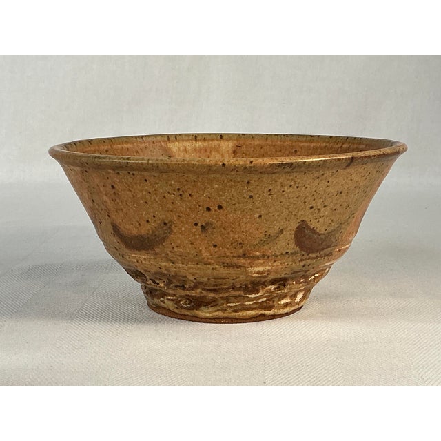 The bowl has a warm, earthy brown glaze with a textured finish, creating a unique and tactile surface. The shape is simple...