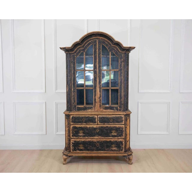 An elegant period Rococo cabinet dating to circa 1820 and featuring beautifully curved lines, glass doors, and refined...