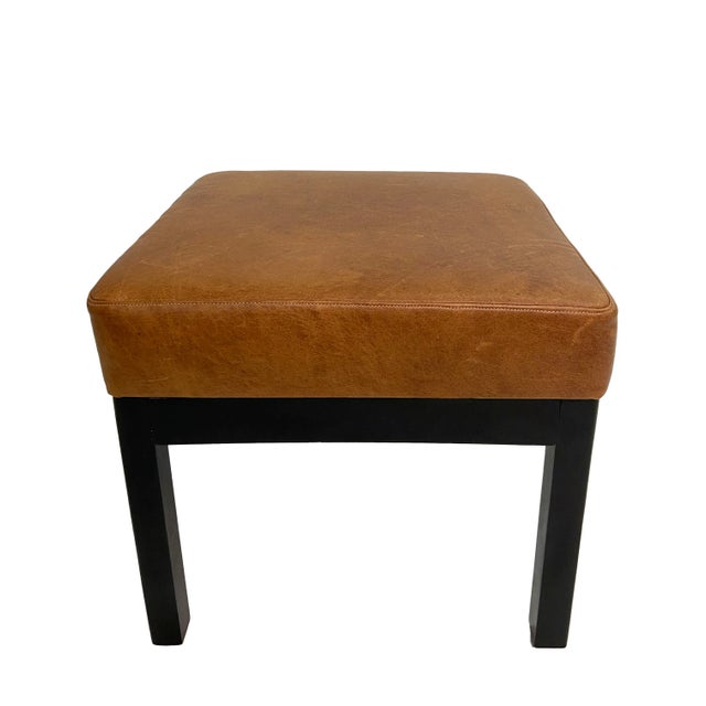 A pair of classic square low stools with cushions upholstered in handsome and mildly distressed brown leather. The solid...