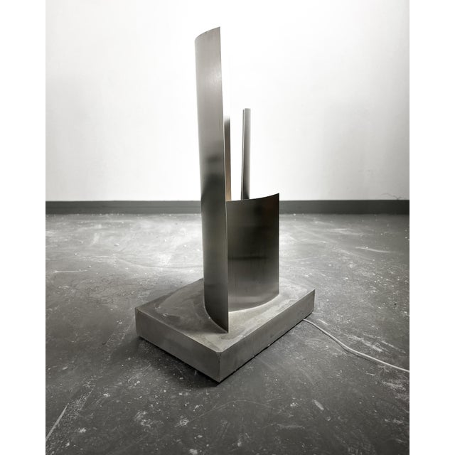 Brushed Stainless Steel Plates, seamlessly placed in a smooth concrete base, illuminated sideways and upwards by...