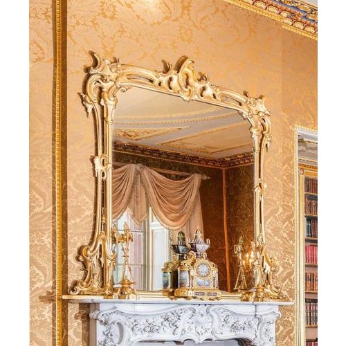 This is a large imposing elegant antique English Rococo revival carved giltwood and gesso overmantel mirror, Circa 1850 in...