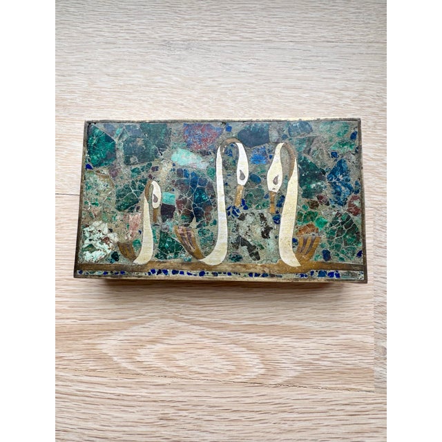 A charming vintage Mexican brass trinket box featuring an intricate semiprecious stone mosaic lid depicting three elegant...