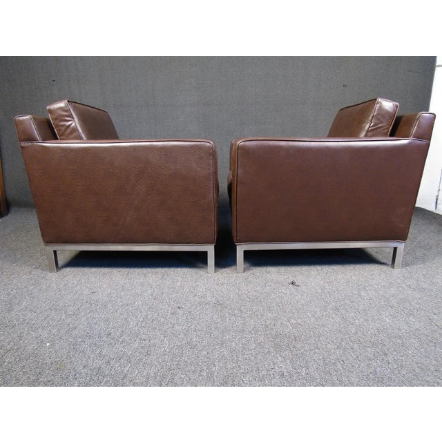 This vintage pair of club chairs is upholstered in a rich brown vinyl that is complemented by metal legs, making them a...