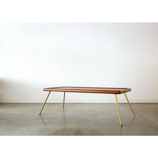 An iconic T.H. Robsjohn Gibbings for Widdicomb brass leg coffee table or bench. A slab of mahogany floats on splayed brass...