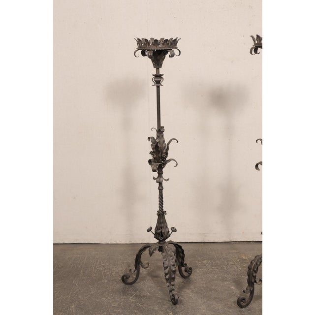 A French pair of black iron single candlestick floor lamps from the mid 20th century. This vintage pair of candle lights...