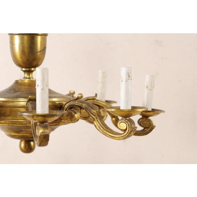 A French gold toned metal eight-light chandelier from the mid 20th century. This vintage chandelier from France features...