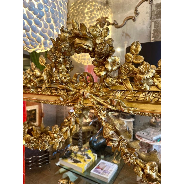 A sizeable ornate French Louis XVI style overmantel mirror. The top crested by a large floral foliate arch above a ribbon...