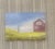 A peaceful countryside scene featuring a red farmhouse and laundry dancing in the breeze beneath an open blue sky. Soft...
