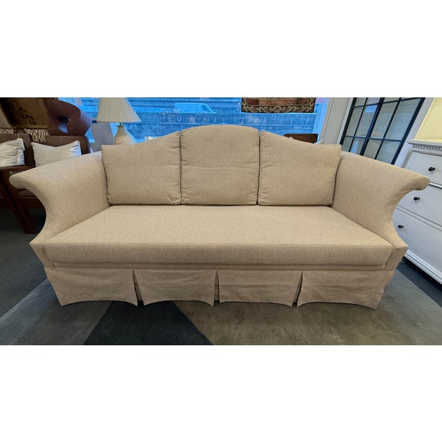 Design Plus Gallery presents a Formal Sofa with Kick Pleat Skirt and Camel Back Frame. The sofa has a light tan upholstery...