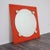 A striking wall mirror made of orange lacquered wood with a circular glass insert and geometric details in relief. An...