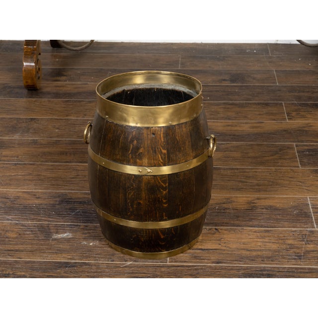 A rustic English turn of the century oak barrel from the early 20th century, with brass braces, and ring handles. Created...