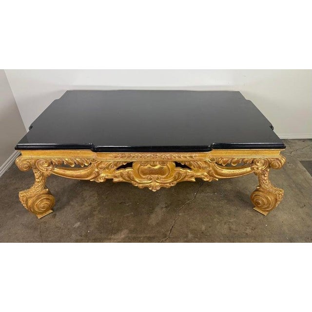 An opulent hand-carved coffee table finished in luminous 22-karat gold leaf, showcasing richly sculpted Baroque-style...