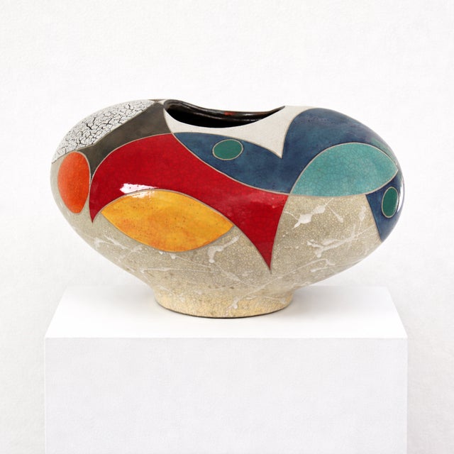 Wide and low, the form spreads outward with a generous, rounded presence. A sandy, crackled ground covers much of the...