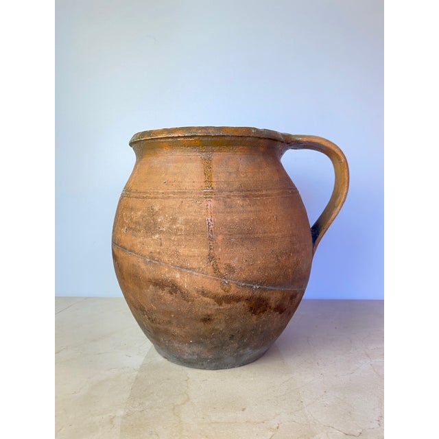 Antique hand-thrown terracotta water jug in a warm, sun-baked terracotta hue, left entirely unglazed to showcase the raw...