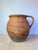 Antique hand-thrown terracotta water jug in a warm, sun-baked terracotta hue, left entirely unglazed to showcase the raw...