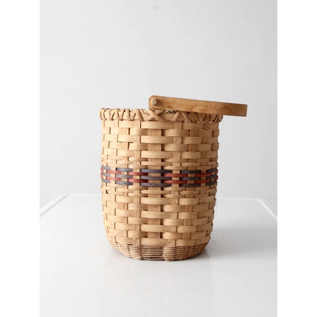 This vintage mid-century woven splint basket has a tall oval shape accented with soft blue and red bands and a graceful...