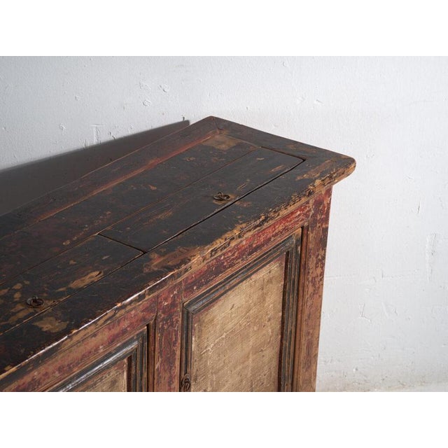 This antique sideboard in elm wood with three doors features framed panels with raised central field and traces of dark...