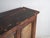 This antique sideboard in elm wood with three doors features framed panels with raised central field and traces of dark...
