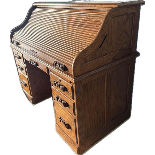 This vintage Postmaster oak roll-top desk features a distinctive curved tambour top and traditional carved wooden drawer...