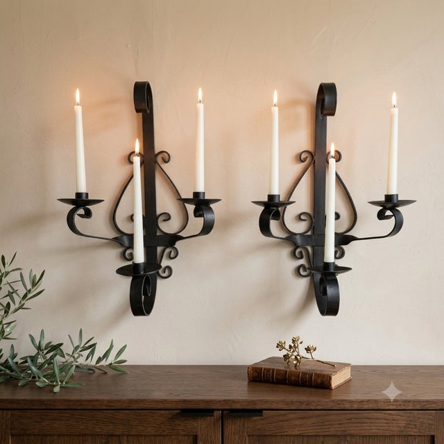 A substantial 1960s pair of black-painted iron wall candle sconces, each designed with three arms for standard taper...