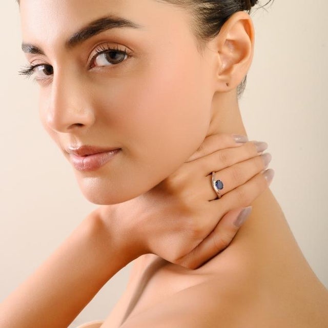 This timeless ring features a captivating 1.1-carat oval-cut blue sapphire, gracefully set in a wavy four-prong design set...