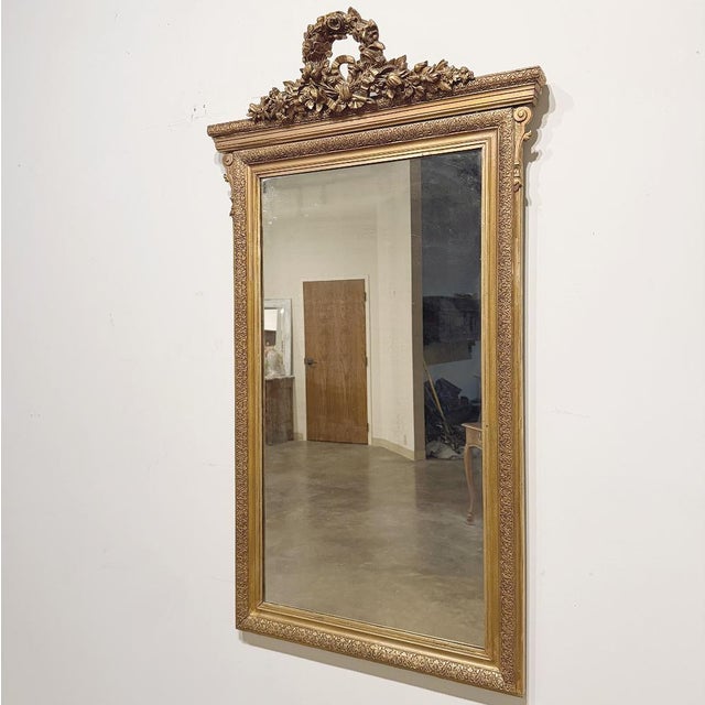 Celebrating the refined symmetry and graceful ornamentation of the Louis XVI period, this elegant French antique mirror...