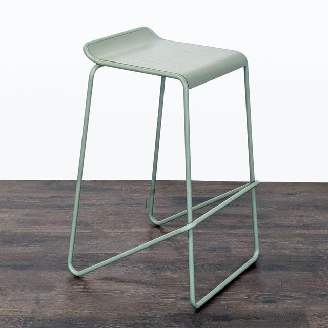 This Blu Dot counter stool features a sleek, modern design with a light green metal frame and a gently curved seat for...
