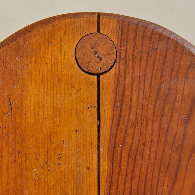 A rustic French wooden stool, crafted circa 1950s. The circular seat is formed from joined solid wood planks, secured with...
